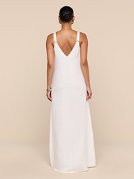 A woman stands facing away against a plain white background, wearing the Didi Maxi Dress—a long, sleeveless linen blend maxi dress in pale pink featuring adjustable straps and a V-shaped back.