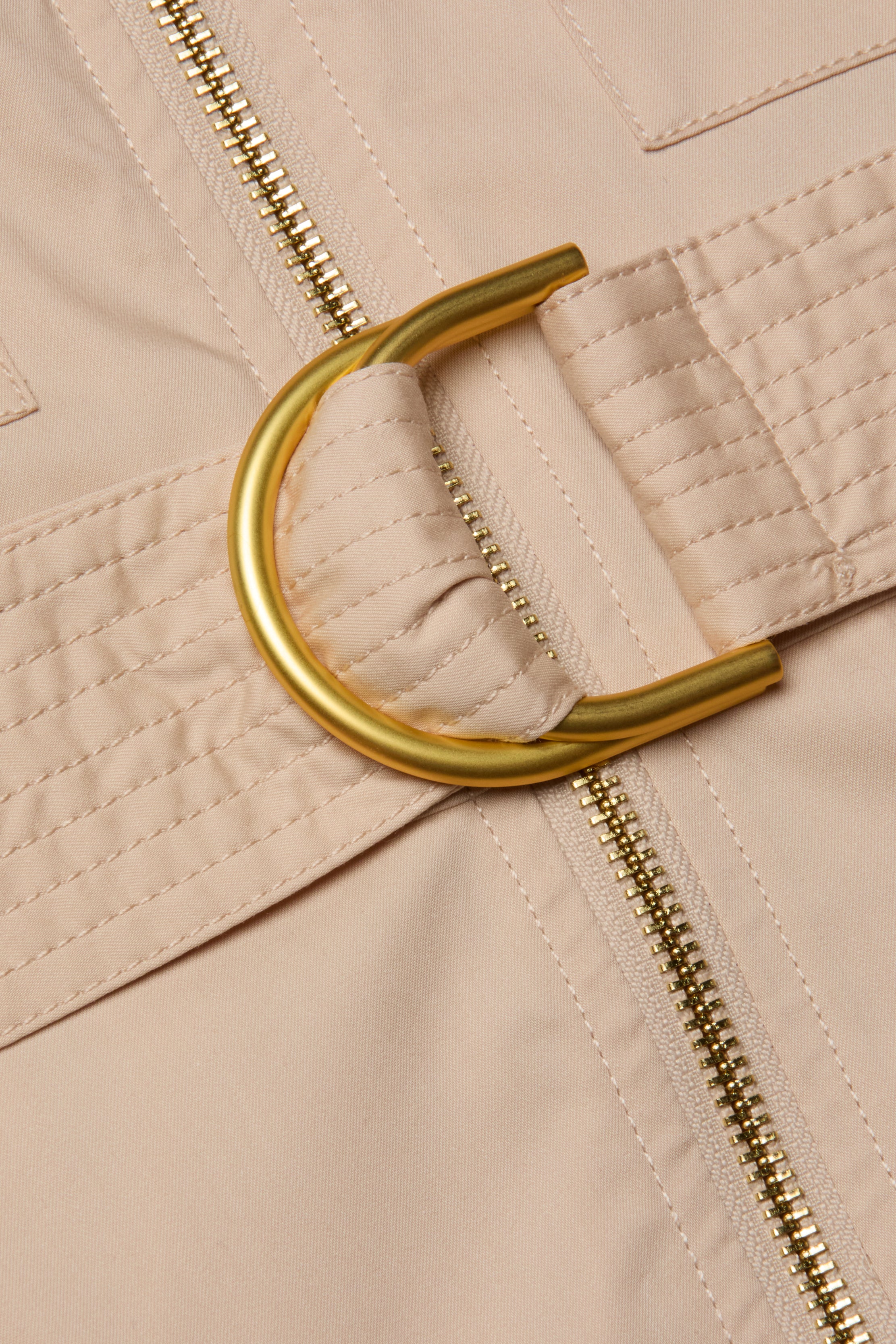 Close-up of the beige fabric from the Callen Shirt Dress, featuring a gold metal D-ring belt, quilted stitching, and a visible gold zipper.