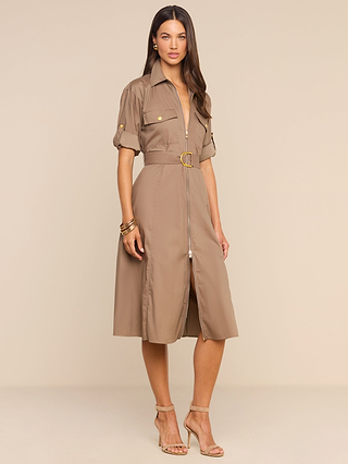 A woman stands in nude heels against a beige background, wearing the Callen Shirt Dress—a belted, short-sleeve, cotton-blend poplin design featuring an exposed front zip and a gold buckle.