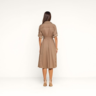 Une femme aux longs cheveux châtains se tient dos à la caméra devant un fond beige. Elle porte la robe-chemise « Callen » — une robe-chemise couleur beige clair, dotée d’une ceinture et d’un col, confectionnée en popeline de coton mélangé et aux manches retroussées —, assortie à des escarpins beiges.