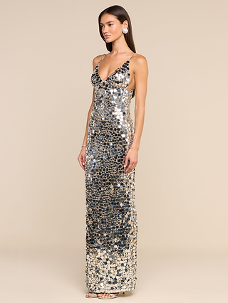 Wearing the Caelith Sequin Gown—a sleeveless, floor-length dress with dazzling sequins and a deep V-neckline—a woman exudes Hollywood glamour as she poses against a plain beige background.