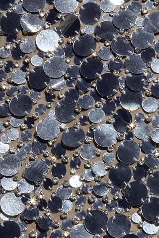 A close-up of shimmering silver sequins and beads scattered across beige fabric, reflecting light to create sparkling highlights reminiscent of classic Hollywood glamour—exquisite details that define the elegance of the Caelith Sequin Gown, perfect for a sophisticated evening ensemble.