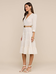 A woman wearing sunglasses, a belted Serafine Midi Dress in lightweight voile, and heeled sandals stands against a plain white background.