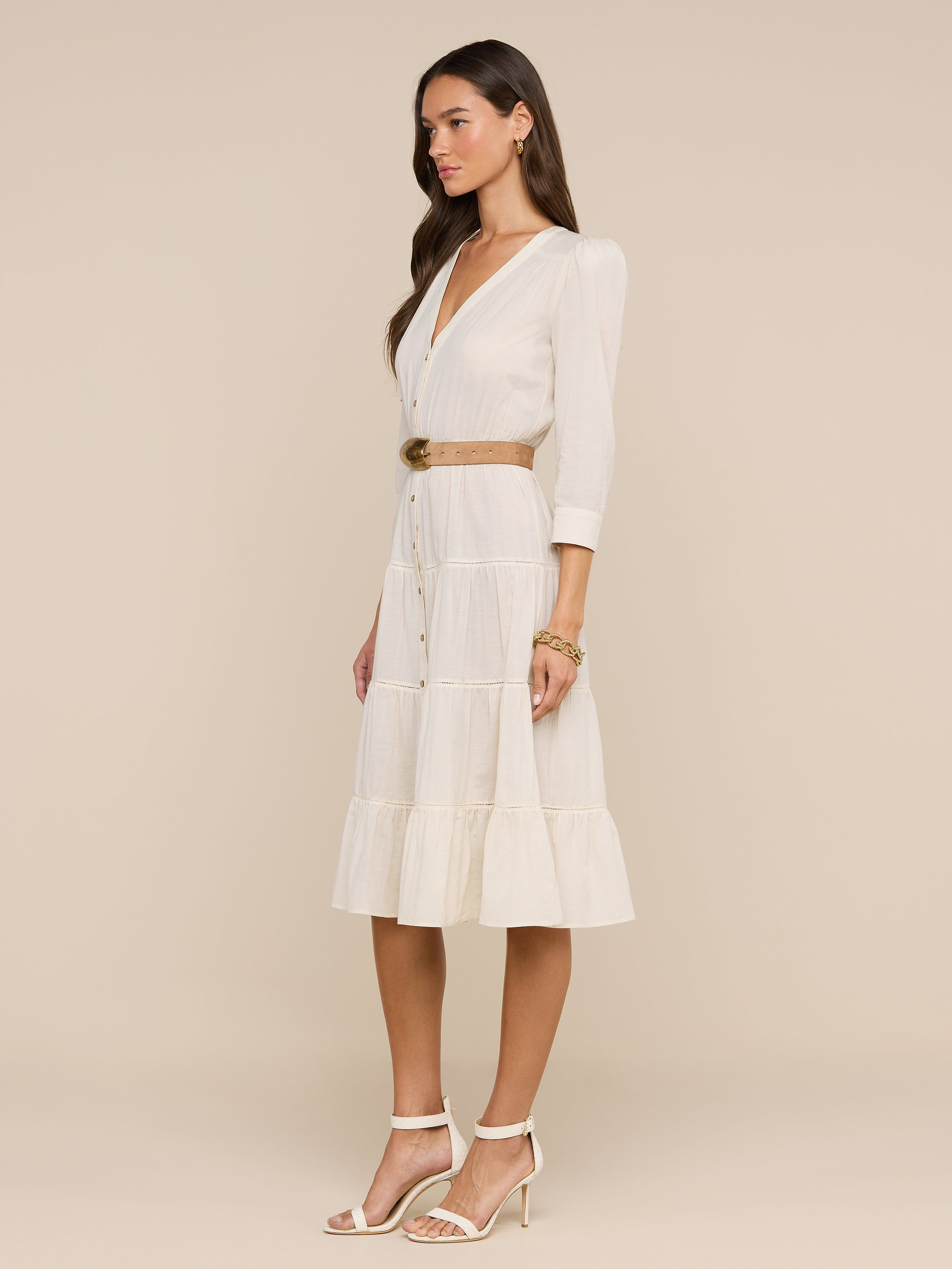 A woman wearing sunglasses, a belted Serafine Midi Dress in lightweight voile, and heeled sandals stands against a plain white background.