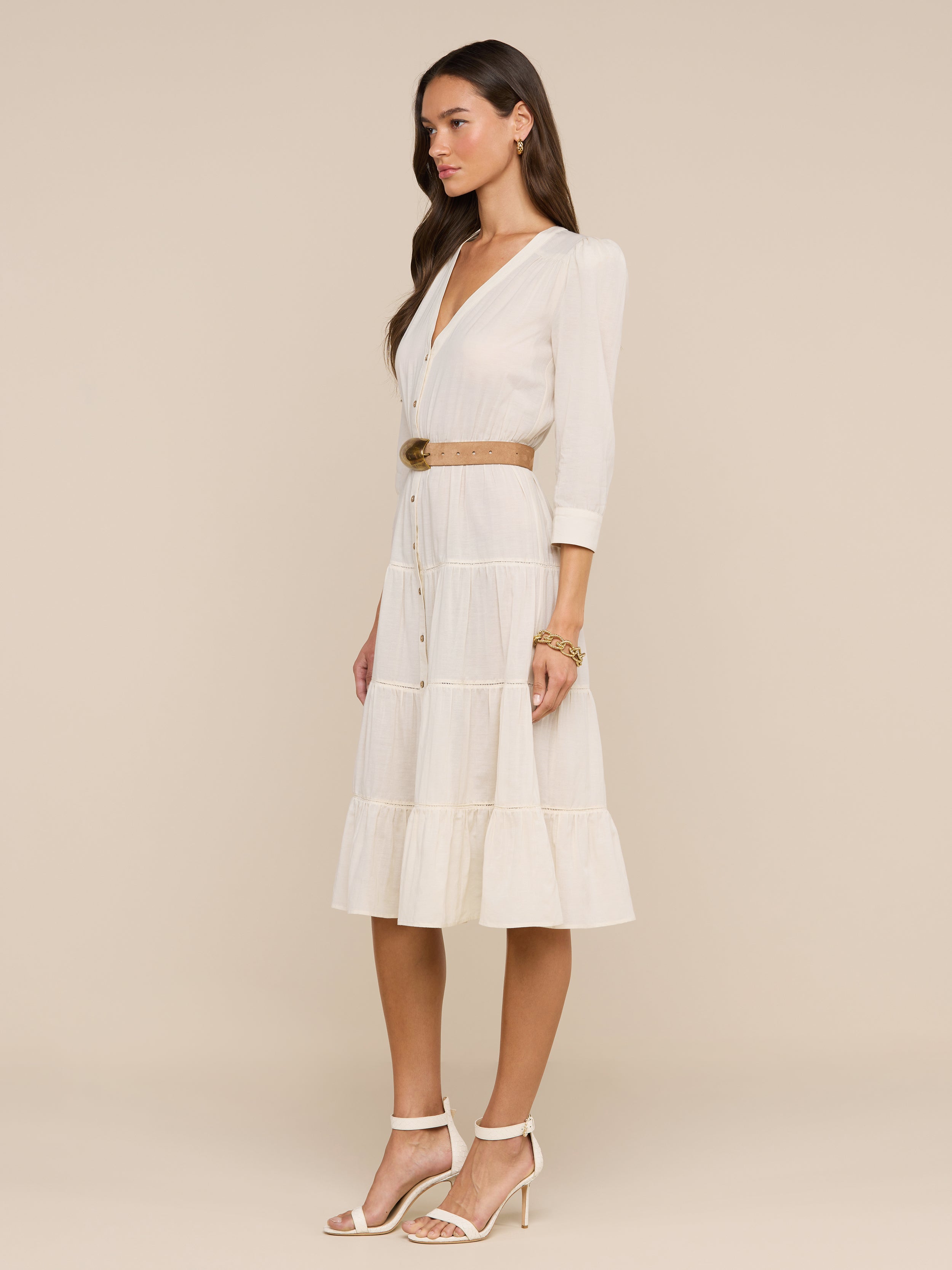 A woman wearing sunglasses, a belted Serafine Midi Dress in lightweight voile, and heeled sandals stands against a plain white background.