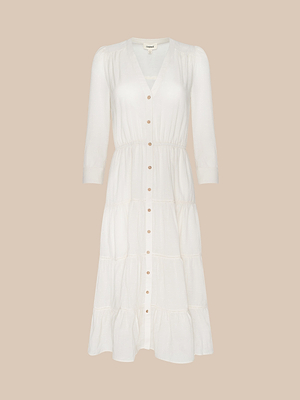 The Serafine Midi Dress is a white, long-sleeve midi with a V-neckline and elastic waist, made from lightweight voile, shown on a plain beige background.