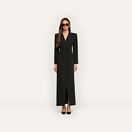 A woman wears a black, floor-length, long-sleeved Vale Tuxedo Dress in a double-breasted style, paired with black pointed-toe heels and sunglasses.