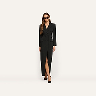 A woman wears a black, long-sleeved, double-breasted Vale Tuxedo Dress with a front slit and black pumps.