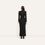Back view of a person wearing a Vale Tuxedo Dress, a floor-length black maxi with structured shoulders and high heels.
