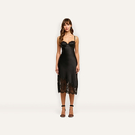 A woman wears the Adrienne Silk Lace Dress, a black silk midi-length slip dress with a corset-style bodice and lace trim at the hem, paired with black ankle-strap heels.