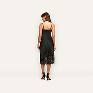 Back view of a woman wearing the black Adrienne Silk Lace Dress, a midi-length slip dress with spaghetti straps and a black lace hem, paired with black high-heeled sandals.