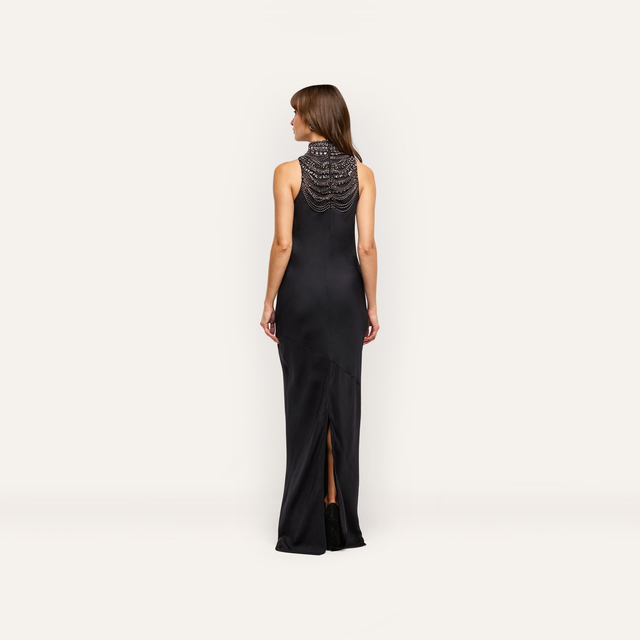 Back view of a woman wearing the black satin Yuan Embellished Gown, featuring a crystal-embellished high-neck collar and a back slit.