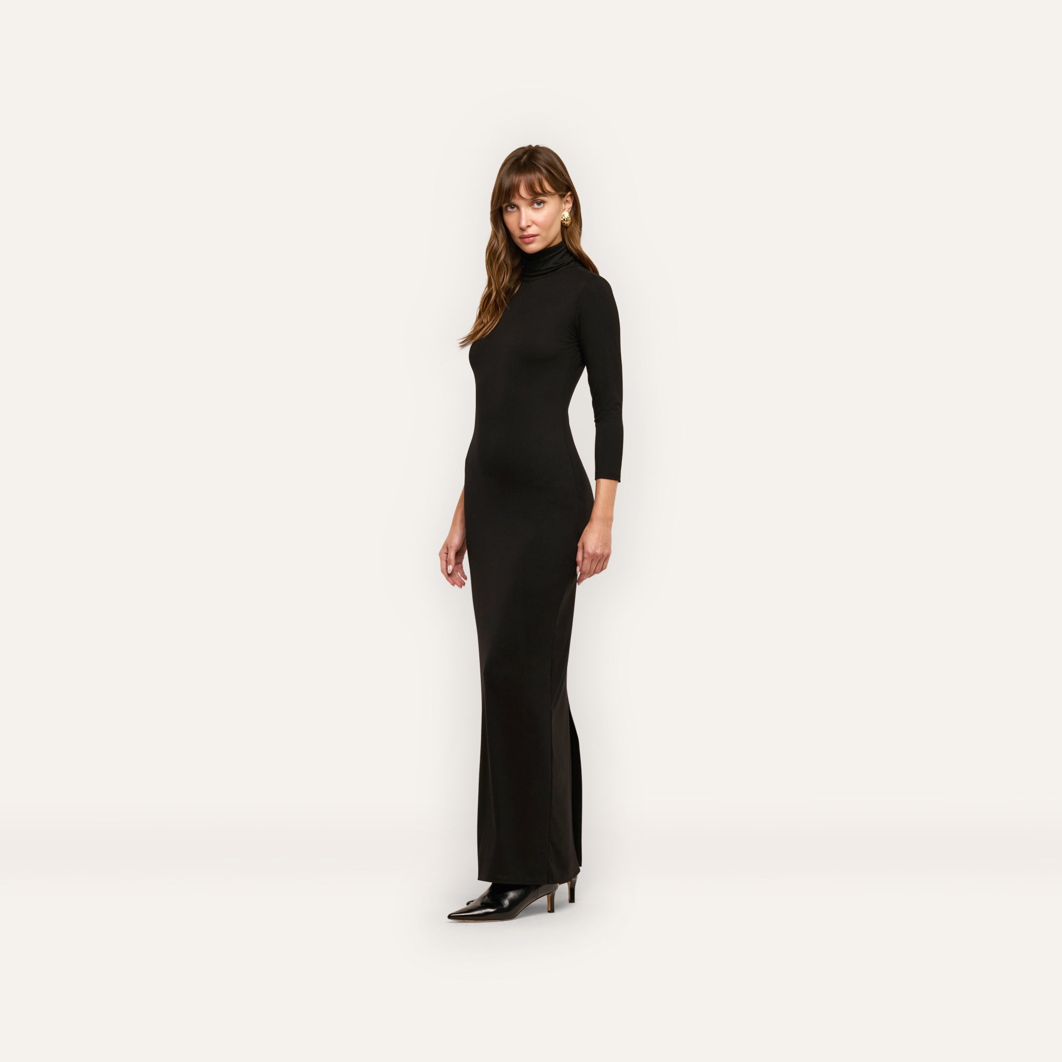 A woman wearing a black three-quarter length sleeve turtleneck Jaesyn Dress and black pointed-toe heels.