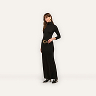 A woman wears the Jaesyn Dress, a black jersey knit turtleneck maxi dress with three-quarter length sleeves and a wide belt featuring a decorative gold buckle.