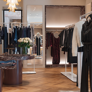 Interior of a clothing store with racks of clothes and a mirror reflecting the room.