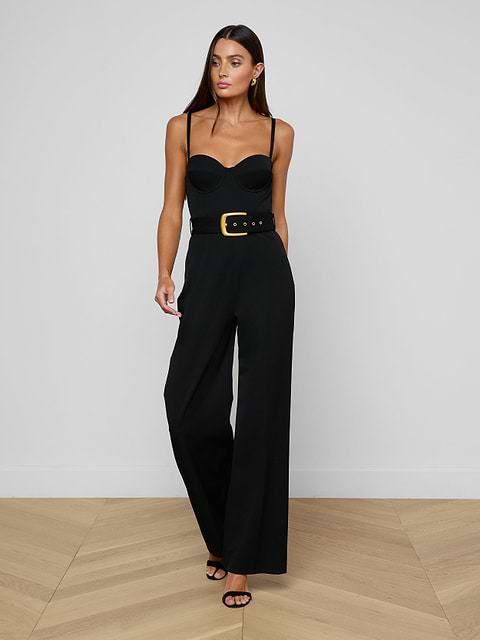 A woman wearing the Jessa Bustier Jumpsuit, crafted from bi-stretch twill with a waist-defining belt, paired with black heels, stands against a plain light background.