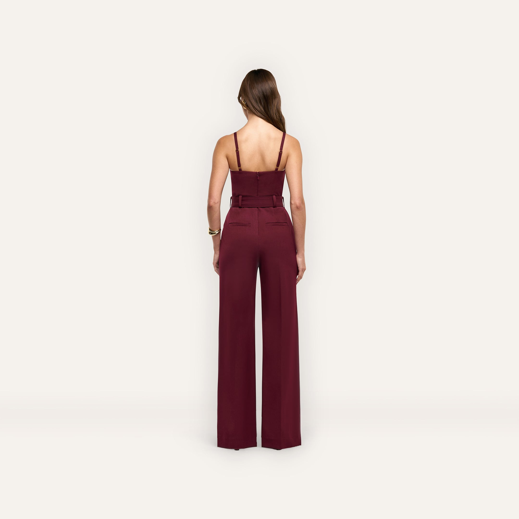Back view of a person wearing a maroon Jessa Bustier Jumpsuit featuring a belted waist and wide-leg trousers.