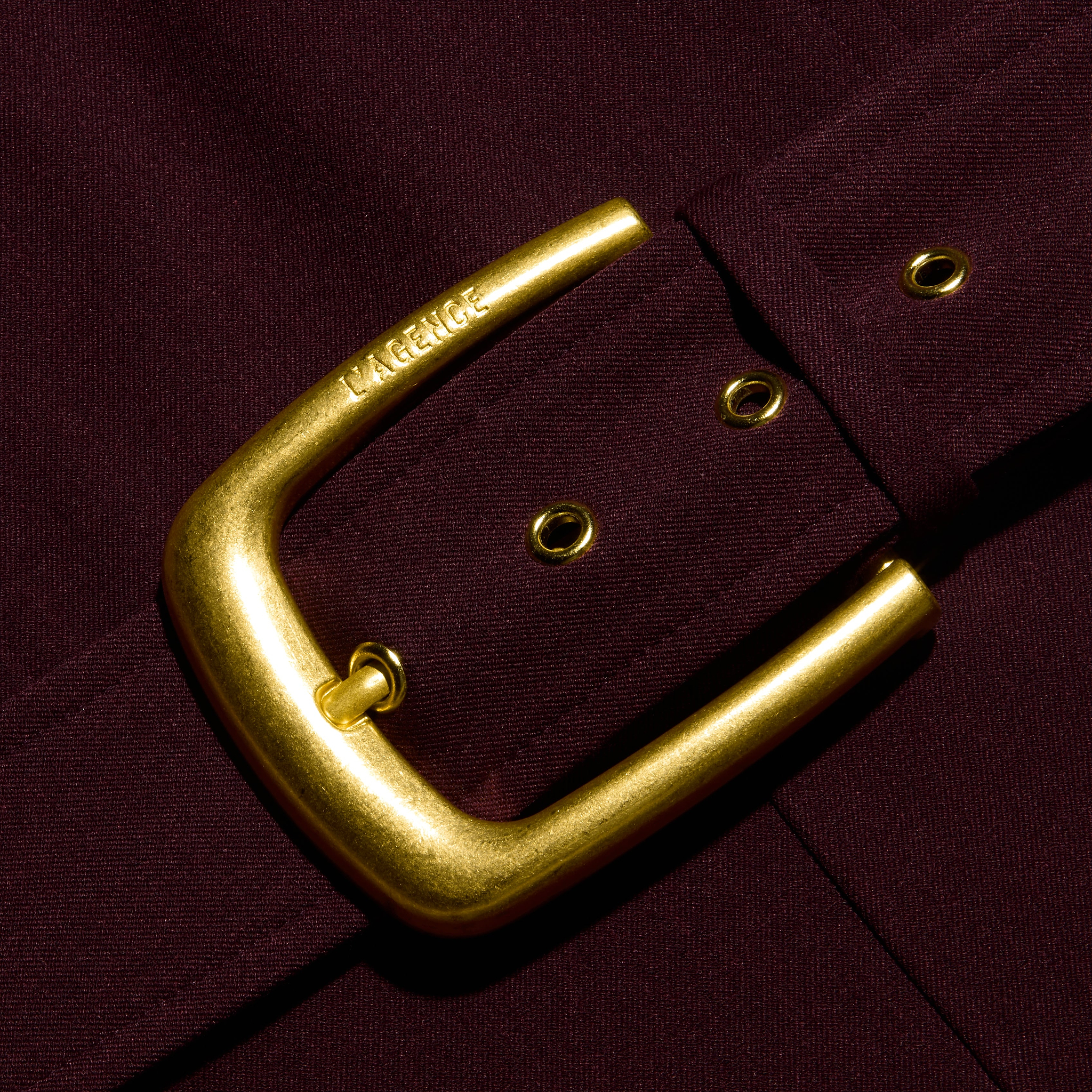 Close-up of a gold-toned belt buckle fastened on a dark burgundy Jessa Bustier Jumpsuit featuring metal grommets.