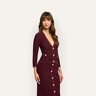 A woman wears a deep burgundy Irvin Pointelle Knit Cardigan with gold buttons over a matching ribbed midi skirt, serving as a lightweight transitional layer.