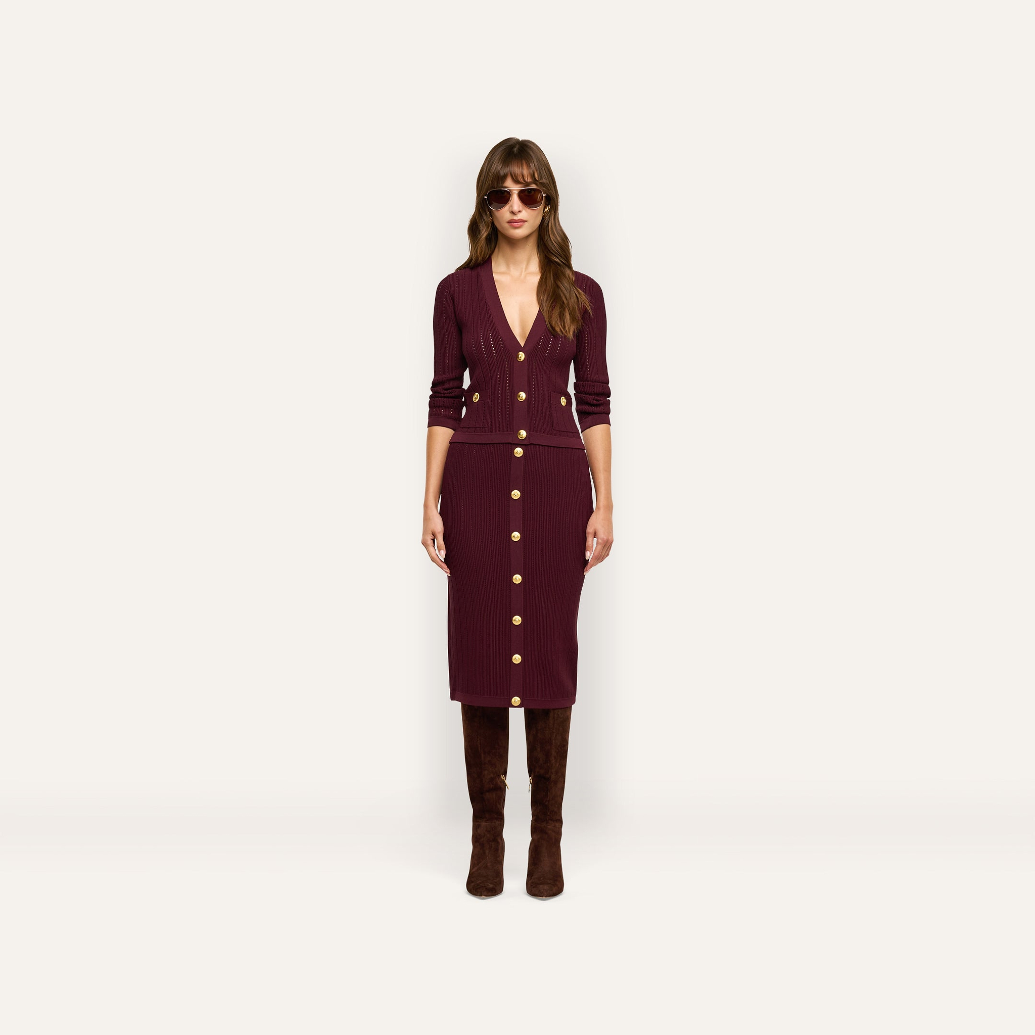 A person wearing a burgundy Irvin Pointelle Knit Cardigan and matching midi skirt with gold buttons, paired with tall brown boots and sunglasses.