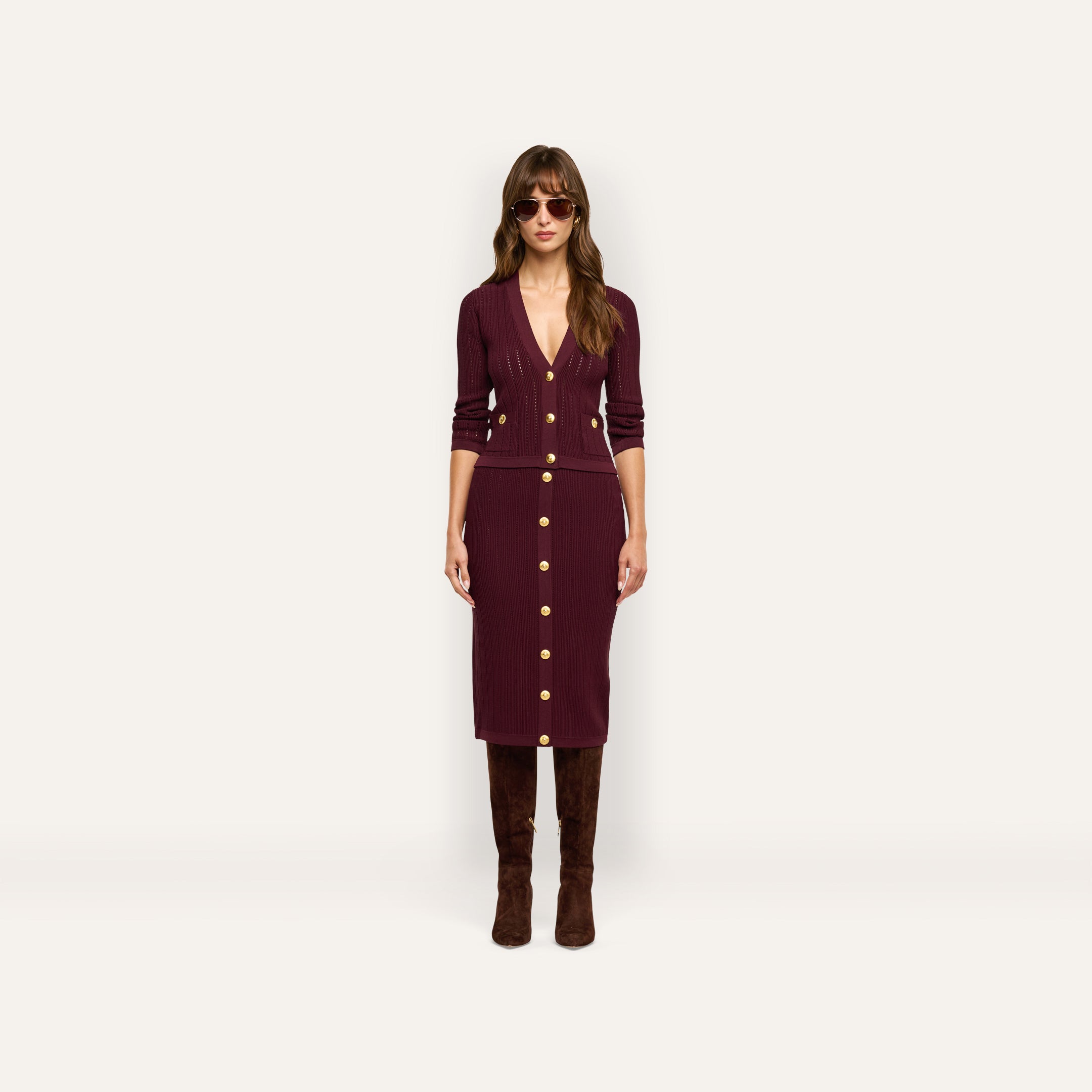 A person wearing a burgundy Irvin Pointelle Knit Cardigan and matching midi skirt with gold buttons, paired with tall brown boots and sunglasses.