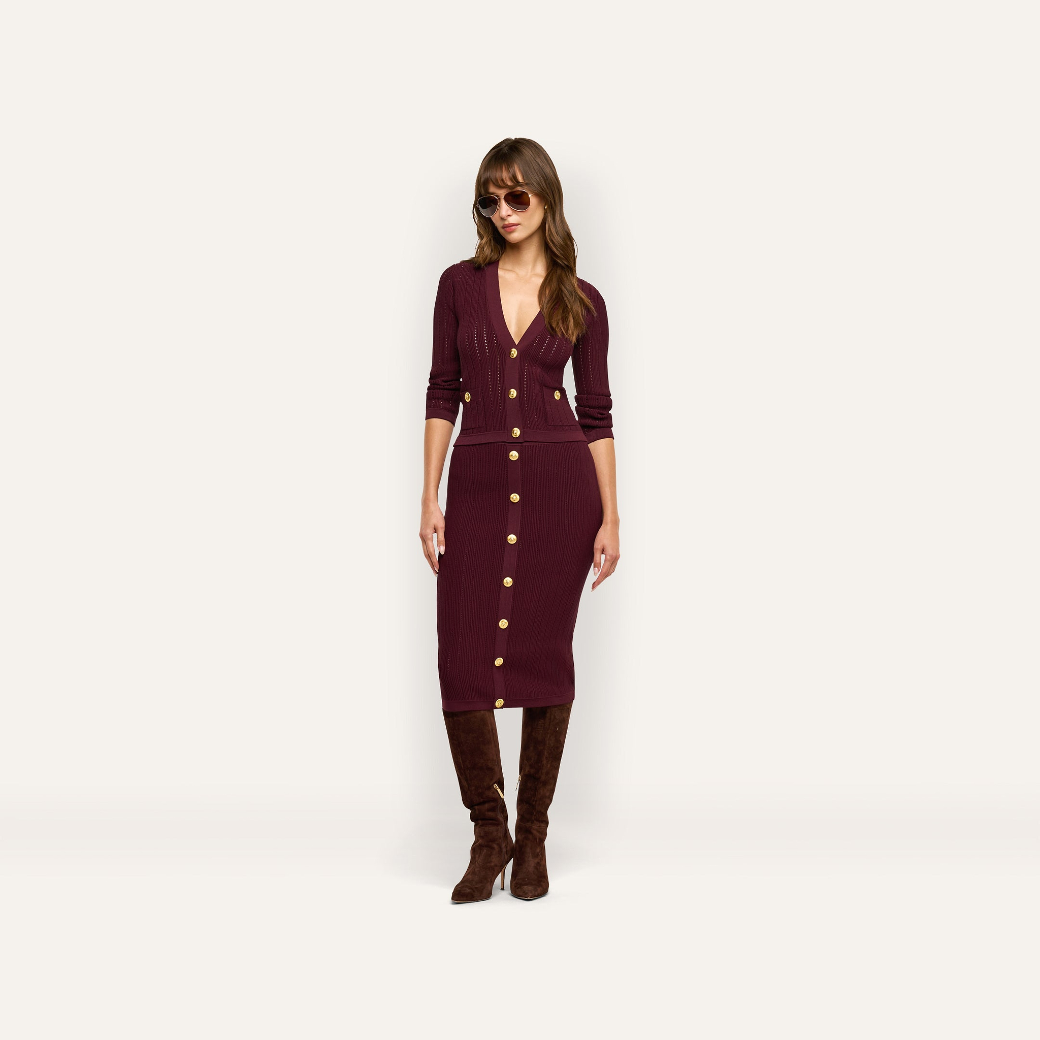 A woman in an Irvin Pointelle Knit Cardigan and matching burgundy pencil skirt, paired with brown suede knee-high boots and sunglasses as a lightweight transitional layer.