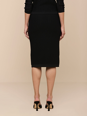 Only the lower body of a woman is visible as she faces away, modeling the Melania Pointelle Knit Skirt—a pull-on, black pointelle knit design with a body-skimming fit—paired with black open-back high-heeled shoes on a light beige background.