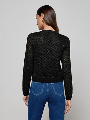 A woman with long brown hair, gold hoop earrings, and blue jeans models the L'AGENCE Blanca Sequin Cardigan, standing with her back to the camera against a plain light background.