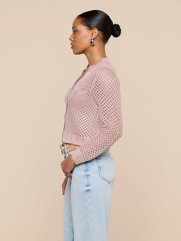 A woman in profile wears the Blanca Sequin Cardigan in adobe rose over light blue jeans, standing against a plain light background. Her hair is styled in a neat bun as she looks straight ahead.