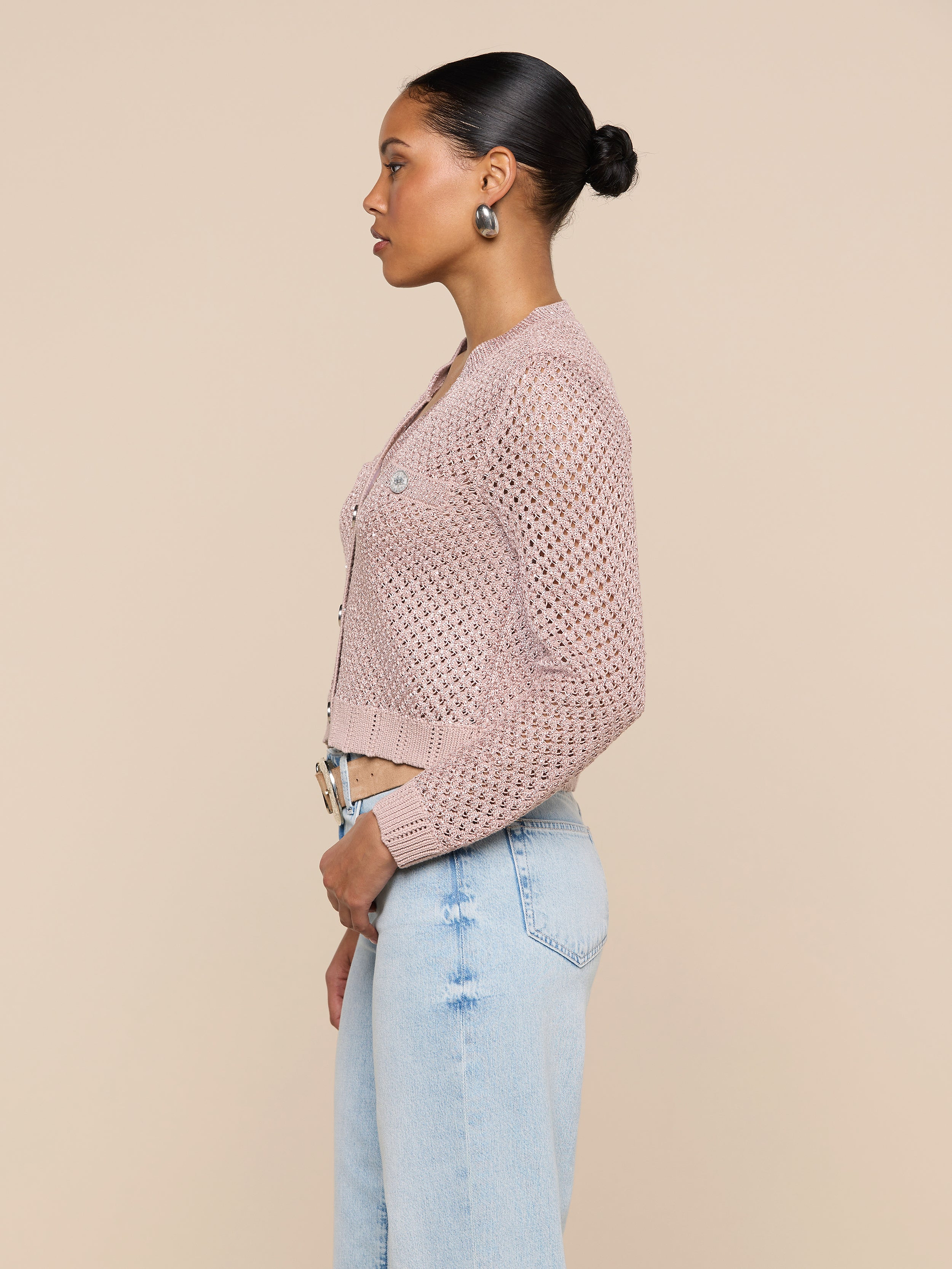 A woman in profile wears the Blanca Sequin Cardigan in adobe rose over light blue jeans, standing against a plain light background. Her hair is styled in a neat bun as she looks straight ahead.