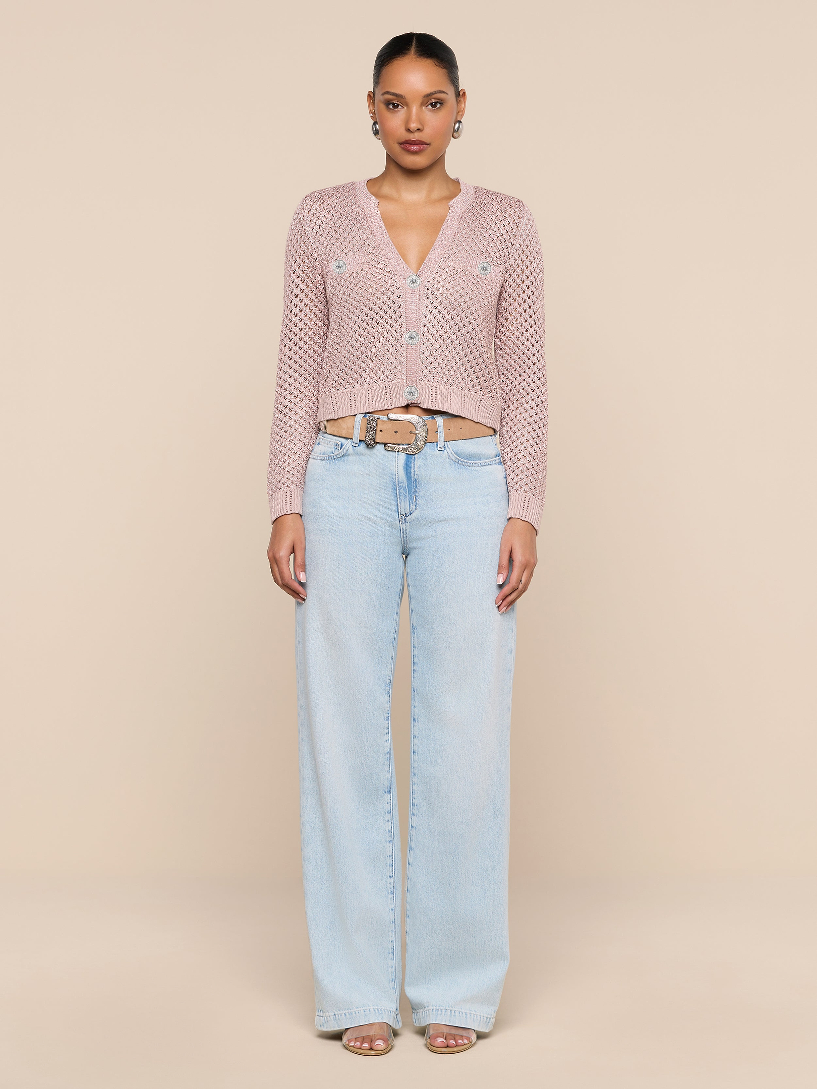 A woman stands against a plain white background, wearing the Blanca Sequin Cardigan in adobe rose, paired with light blue wide-leg jeans, a beige belt, hoop earrings, and open-toed sandals.