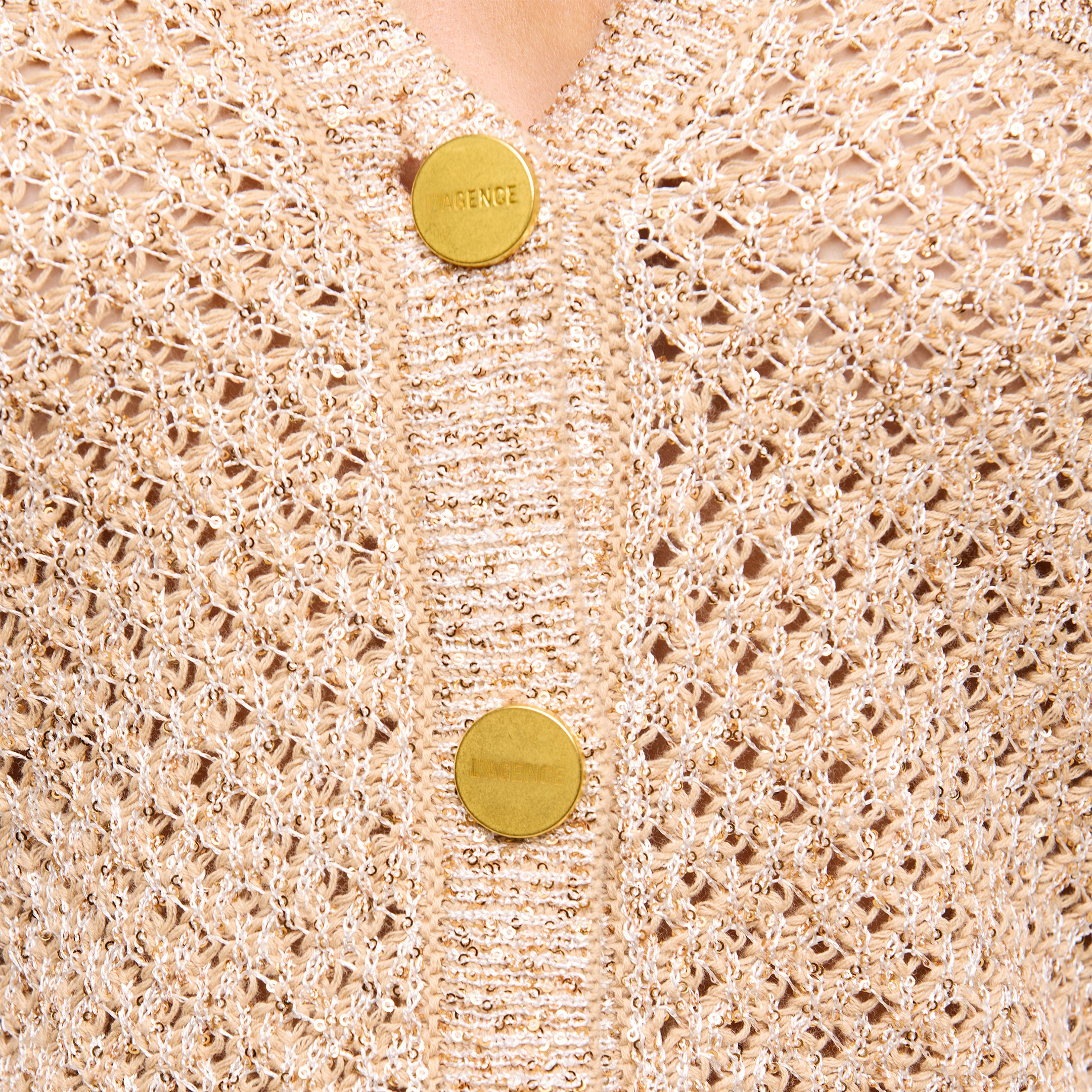 Close-up of the Blanca Sequin Cardigan—a neutral tan, lightweight layer featuring a textured open weave and two large gold buttons, with FRENCE engraved on the top button.