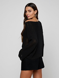 Woman with long brown hair poses in the relaxed-fit Ethan Knit Pullover and black shorts, looking over her shoulder at the camera. She pairs the look with large hoop earrings against a plain light background.