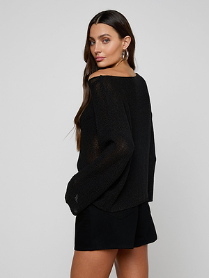 Woman with long brown hair poses in the relaxed-fit Ethan Knit Pullover and black shorts, looking over her shoulder at the camera. She pairs the look with large hoop earrings against a plain light background.