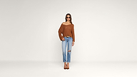Woman wearing sunglasses, a loose brown sweater, ripped light blue jeans, and brown heels stands against a plain white background, looking straight ahead.