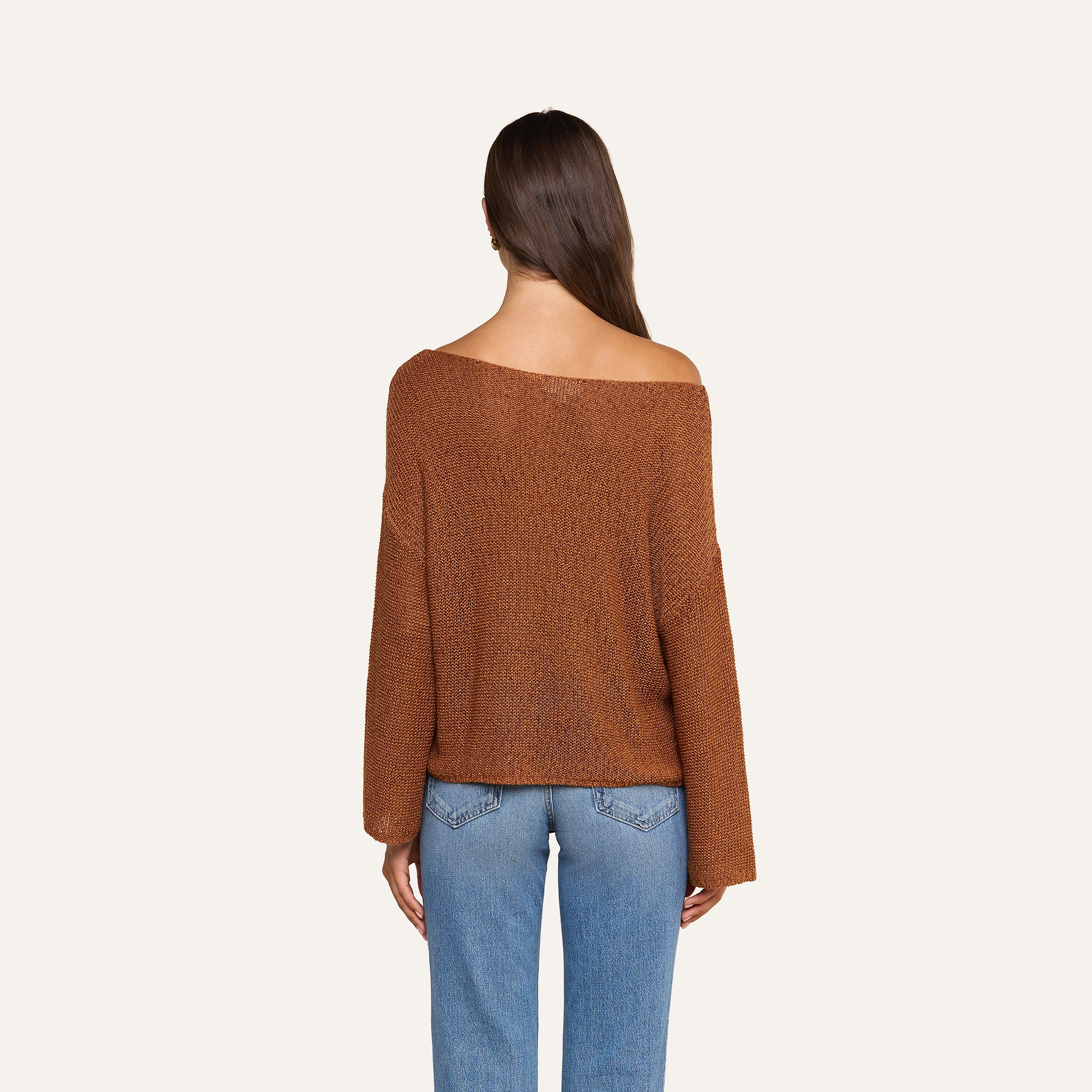 긴 갈색 머리를 한 사람이 넉넉한 핏의 ‘Ethan Knit Pullover’와 청바지를 입고, 무늬 없는 베이지색 배경을 등지고 카메라를 등진 채 서 있다.