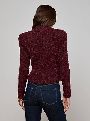 A woman stands with her back to the camera against a light gray background, wearing the Bethany Knit Blazer by L'AGENCE in maroon and dark blue jeans.