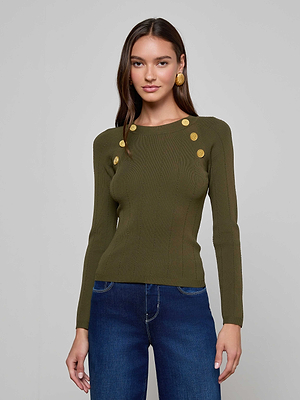 A woman with long brown hair wears the L'AGENCE Gretchen Pullover, a fitted deep olive crewneck sweater with gold shoulder buttons, paired with blue jeans. She stands against a plain light gray background, smiling slightly at the camera.