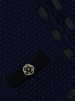 Close-up of the Astor Cardigan by L'AGENCE in midnight blue, featuring Parisian-inspired elegance with textured fabric, black trim, gold floral button, and decorative ribbon woven through.