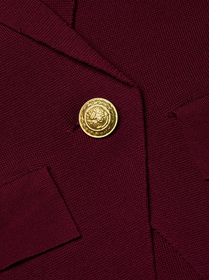 Close-up of the Chamberlain Knit Blazer by L'AGENCE in maroon, showcasing a shiny gold embossed button beside the pocket flap.