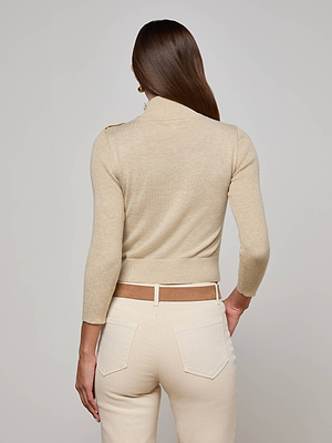 A person with long brown hair is shown from the back wearing the L’AGENCE Kamdyn Cropped Sweater in light beige and cream-colored pants. The outfit features ribbed texture, visible back pockets, and belt loops against a plain background.