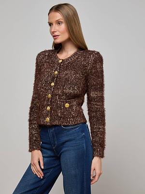 A woman with long, straight hair poses against a plain backdrop wearing the Una Knit Cardigan, featuring textured knit fabric and gold buttons, paired with blue jeans. One hand rests relaxed by her side.