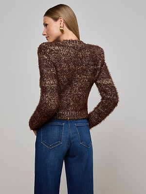 A woman with straight, light brown hair models the Una Knit Cardigan in brown with blue jeans. She stands with her back to the camera, head turned to the side, displaying gold earrings against a plain light background.