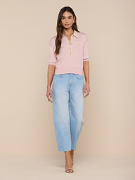 A woman stands facing forward, wearing the Masaki Cropped Sweater in light pink paired with light blue wide-leg jeans. She has long brown hair and is wearing open-toe heels against a plain white background.