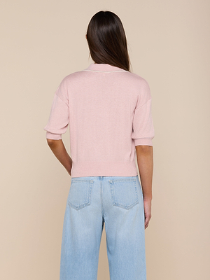 A person with long brown hair is seen from behind in a beige setting, wearing a light pink Masaki Cropped Sweater and light blue high-waisted jeans.