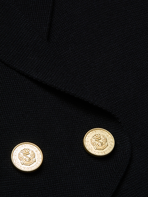 Close-up of the Zadie Knit Vest in black, cropped length, with two shiny gold buttons engraved with a wreath and emblem. Minimalist glamour is emphasized by the buttons on overlapping flaps.