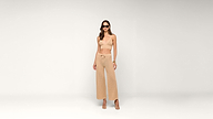 Woman in tan crochet crop top, high-waisted wide-leg pants, and heels stands against a plain white background. She wears sunglasses, holds a handbag, and has wavy hair.