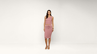 A woman stands in a studio wearing a sleeveless pink knit top and matching skirt with a drawstring waist, paired with heeled sandals against a plain white background.
