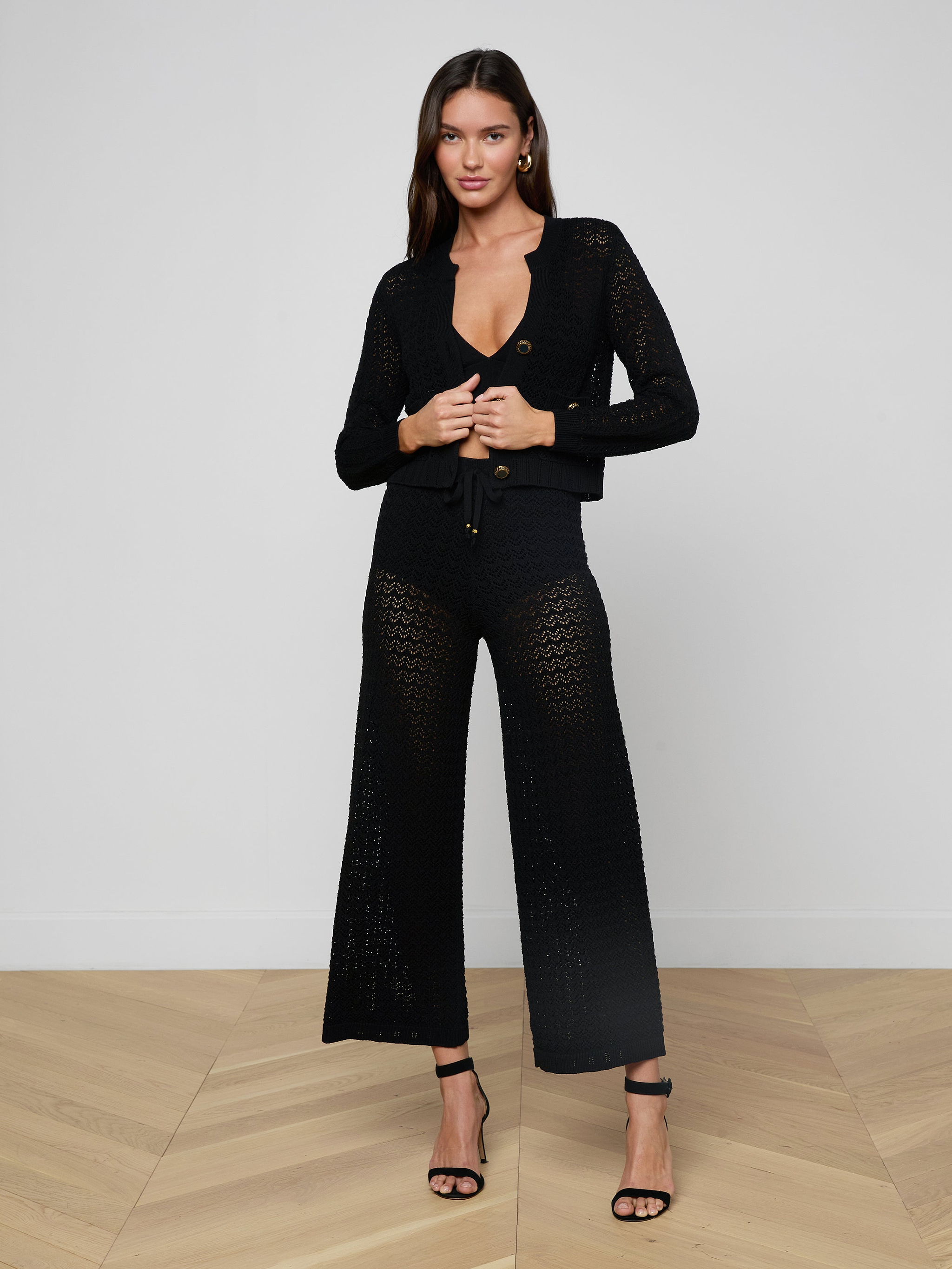 A woman stands against a plain light background wearing the Orla Pointelle Knit Cardigan paired with matching wide-leg pants and black high-heeled sandals.