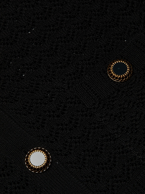 Close-up of the Orla Pointelle Knit Cardigan’s textured black fabric with two round buttons, each featuring gold braided edges—one with a black center and one with a white center.
